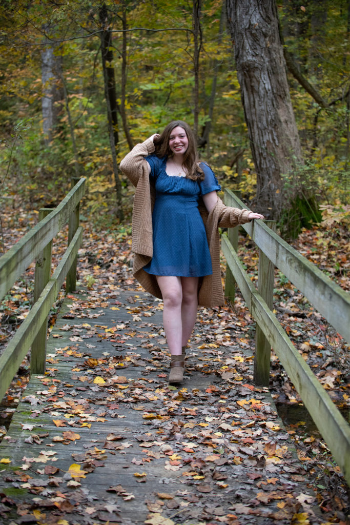 Fall senior portrait with fallen leaves and wooden bridge