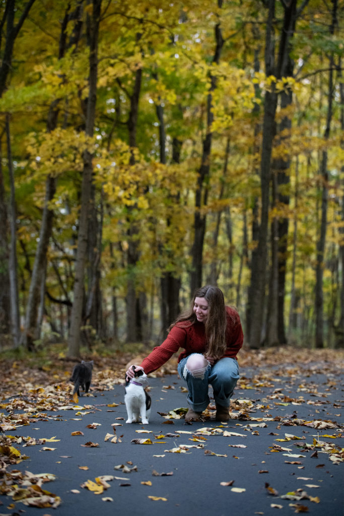 Senior portrait of girl petting a cat on paved trail through woods