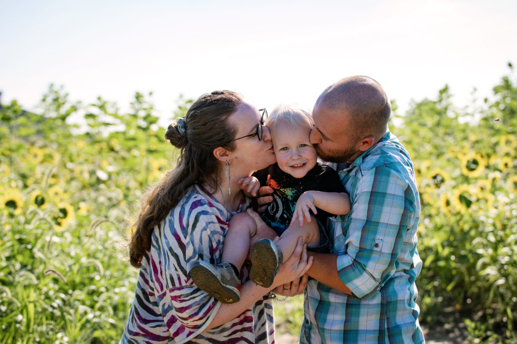 Mom and dad kissing toddler in sunflower field